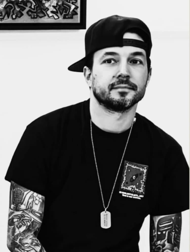 Black-and-white portrait of Yan Lortie, wearing a backwards cap, with tattooed forearms visible